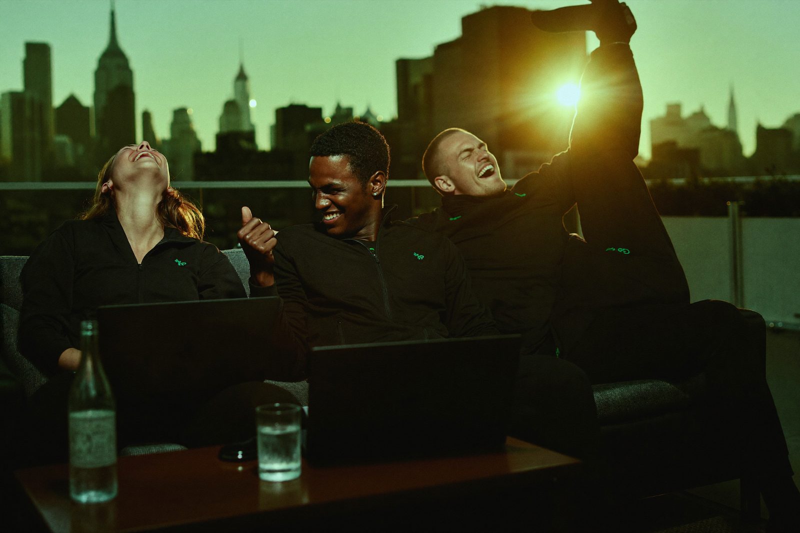 Three members on a hotel rooftop at golden hour, laptops closed, laughing.